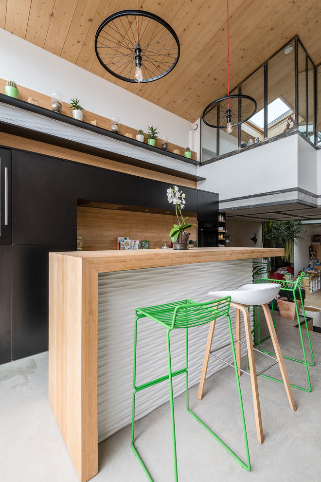 Diseño de cocina contemporánea de tamaño medio abierta con puertas de armario negras, encimera de madera, salpicadero marrón, suelo de cemento, una isla y barras de cocina