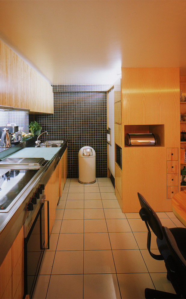 パリにある高級なコンテンポラリースタイルのおしゃれなキッチン (一体型シンク、フラットパネル扉のキャビネット、淡色木目調キャビネット、ステンレスカウンター、黒いキッチンパネル、セラミックタイルのキッチンパネル、シルバーの調理設備、セラミックタイルの床、白い床) の写真