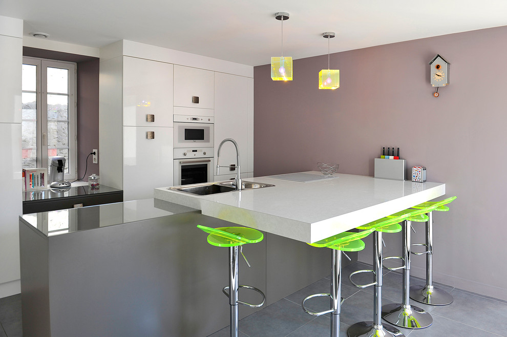 Foto på ett mellanstort funkis kök, med en nedsänkt diskho, släta luckor, vita skåp, vita vitvaror, en köksö, klinkergolv i keramik och grått golv