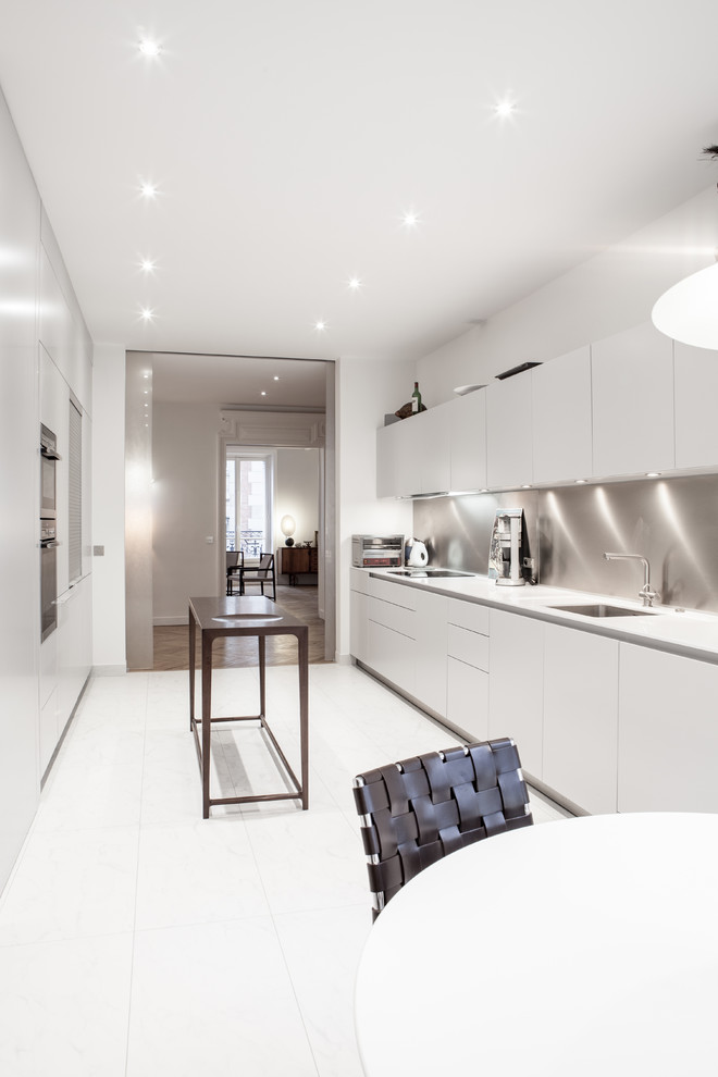 Réalisation d'une grande cuisine ouverte parallèle design avec des portes de placard blanches, une crédence blanche, un électroménager blanc et un sol blanc.