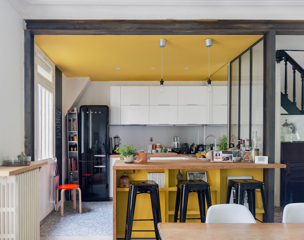 Inspiration för små moderna kök, med en dubbel diskho, luckor med profilerade fronter, vita skåp, träbänkskiva, grått stänkskydd, stänkskydd i metallkakel, svarta vitvaror, cementgolv, en köksö och flerfärgat golv