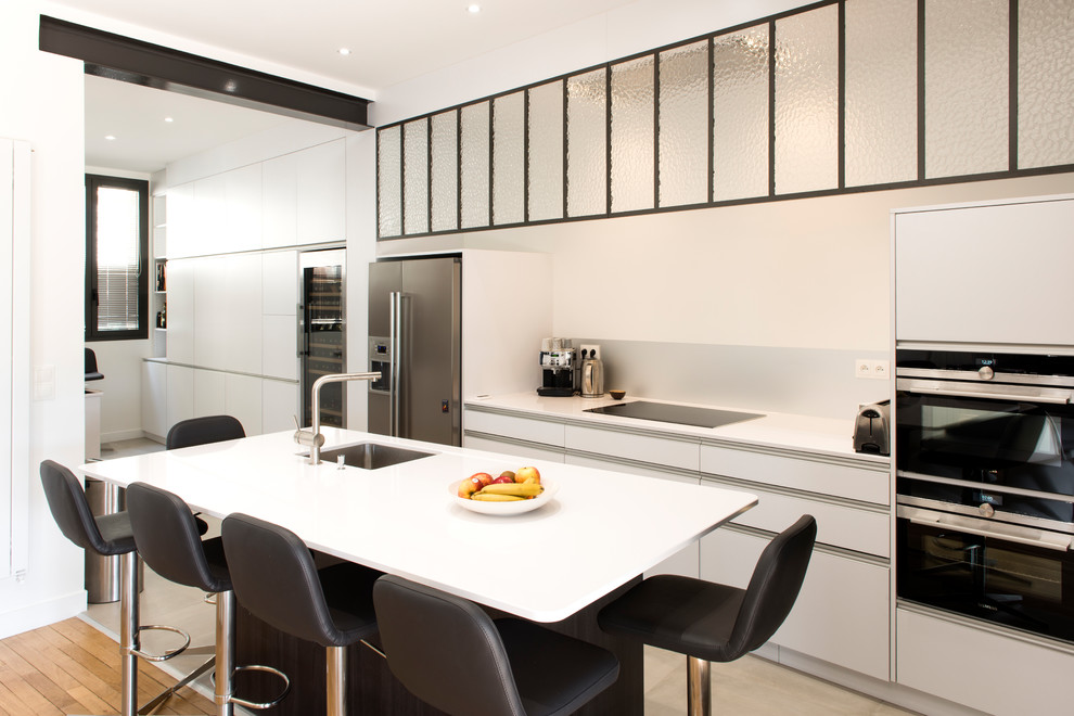 Contemporary kitchen in Le Havre with a single-bowl sink, white cabinets, composite countertops, white splashback, stainless steel appliances, an island, flat-panel cabinets and beige floors.
