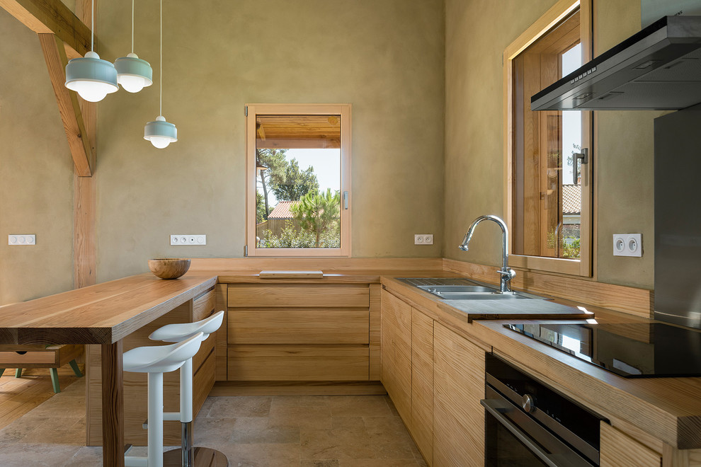Cette image montre une cuisine ouverte rustique en U et bois clair avec un placard à porte plane, un plan de travail en bois, un sol en travertin, un évier 2 bacs, une péninsule et un sol beige.