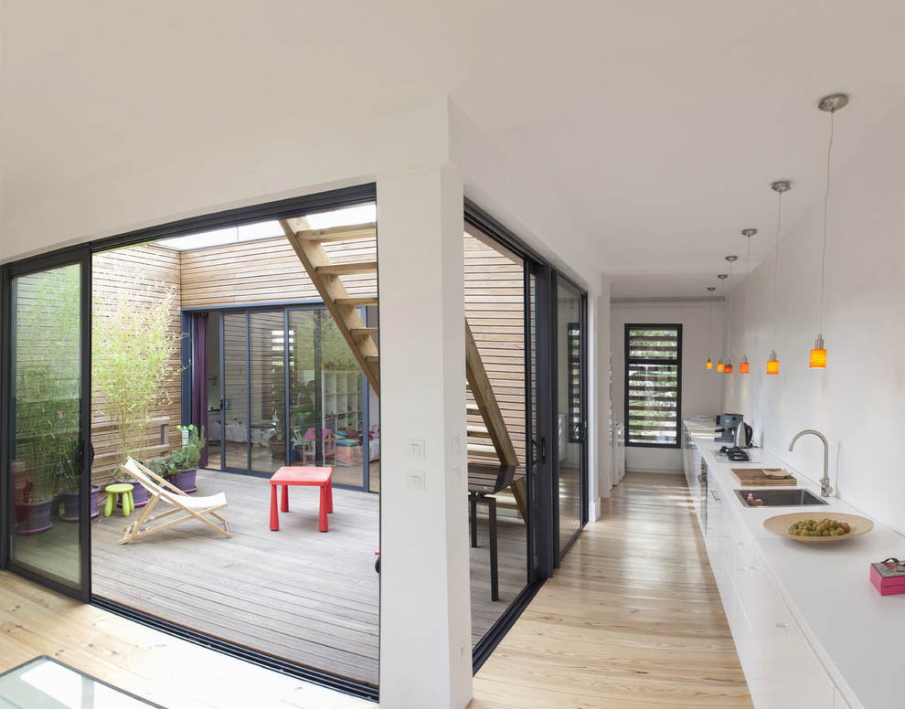 Идея дизайна: прямая кухня-гостиная среднего размера в современном стиле с накладной мойкой, плоскими фасадами, белыми фасадами и светлым паркетным полом без острова
