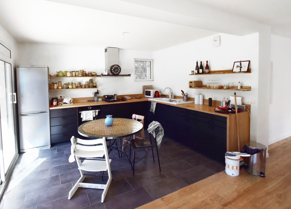 Bild på ett mellanstort funkis brun brunt kök, med en enkel diskho, luckor med profilerade fronter, svarta skåp, träbänkskiva, brunt stänkskydd, stänkskydd i trä, rostfria vitvaror och cementgolv