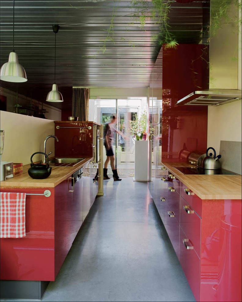 Idee per una cucina industriale di medie dimensioni con ante a filo, ante rosse, top in legno, elettrodomestici bianchi, pavimento in cemento e paraspruzzi grigio