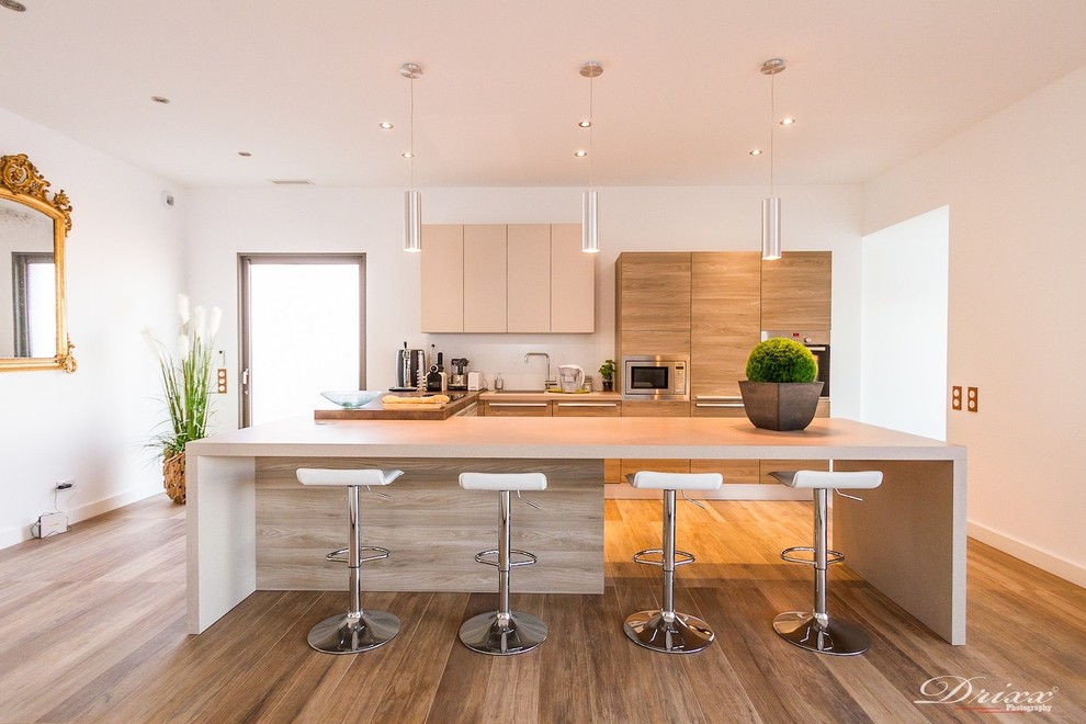 Offene, Mittelgroße Moderne Küche in U-Form mit hellbraunen Holzschränken, Elektrogeräten mit Frontblende und braunem Holzboden in Montpellier