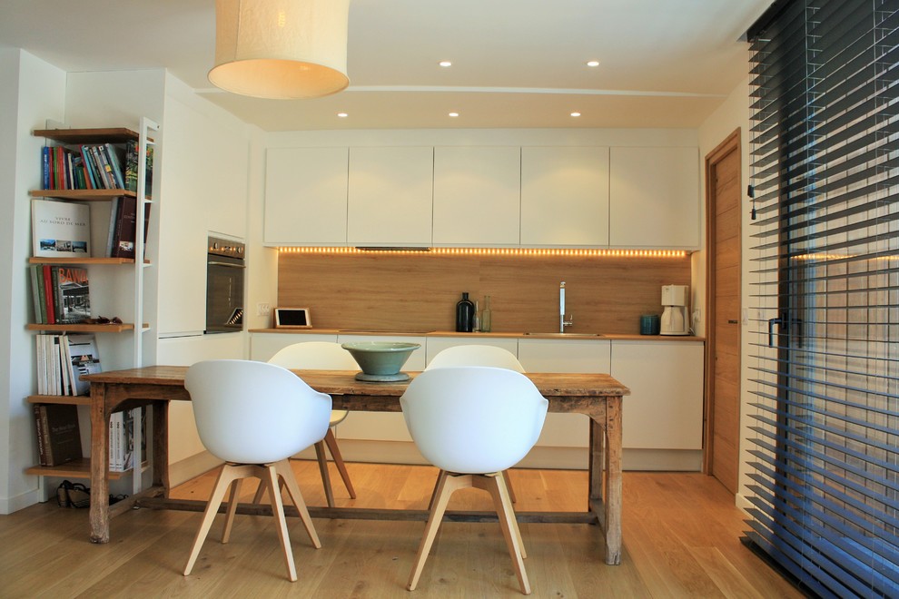 This is an example of a contemporary l-shaped kitchen/diner in Other with flat-panel cabinets, white cabinets, brown splashback, medium hardwood flooring and brown floors.