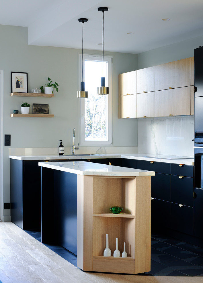 Cette photo montre une cuisine tendance en L avec un évier encastré, un placard à porte affleurante, des portes de placard noires, une crédence blanche, un électroménager noir, îlot et un sol noir.