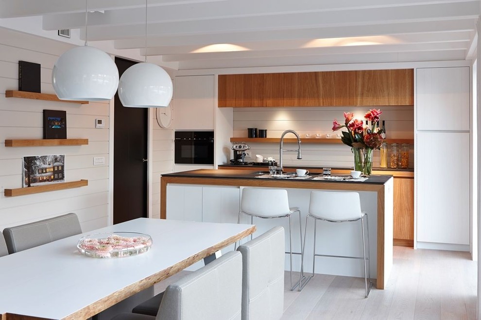 Zweizeilige, Große Retro Wohnküche mit flächenbündigen Schrankfronten, hellbraunen Holzschränken, Küchengeräten aus Edelstahl, hellem Holzboden und Kücheninsel in Paris