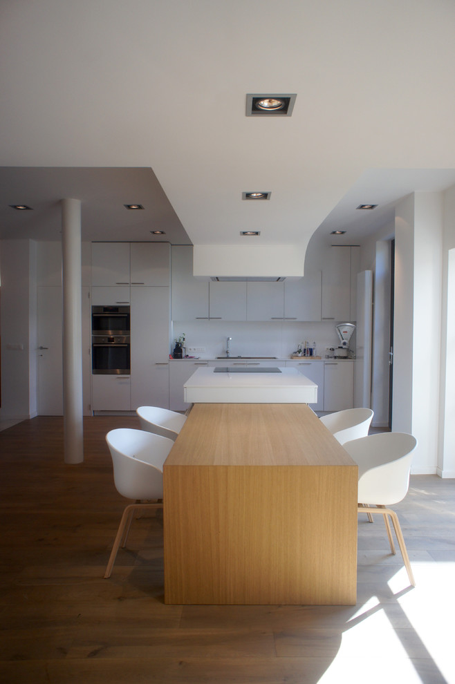 Bild på ett stort funkis linjärt kök med öppen planlösning, med en integrerad diskho, granitbänkskiva, vitt stänkskydd, ljust trägolv, en köksö, vita skåp och integrerade vitvaror
