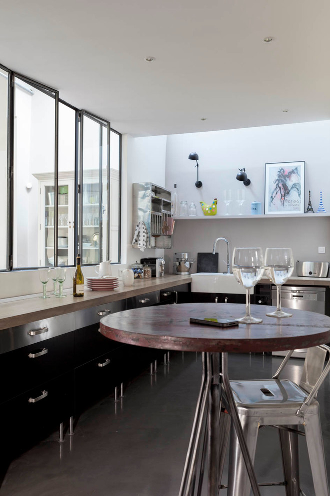Inspiration for a large urban u-shaped open plan kitchen in Paris with a belfast sink, beaded cabinets, black cabinets, wood worktops, white splashback, integrated appliances, concrete flooring, no island, grey floors and beige worktops.