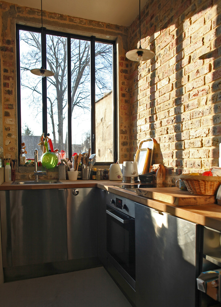 Immagine di una cucina design di medie dimensioni con lavello sottopiano, ante lisce, top in legno, paraspruzzi beige, paraspruzzi in mattoni, pavimento in cemento, nessuna isola e pavimento grigio
