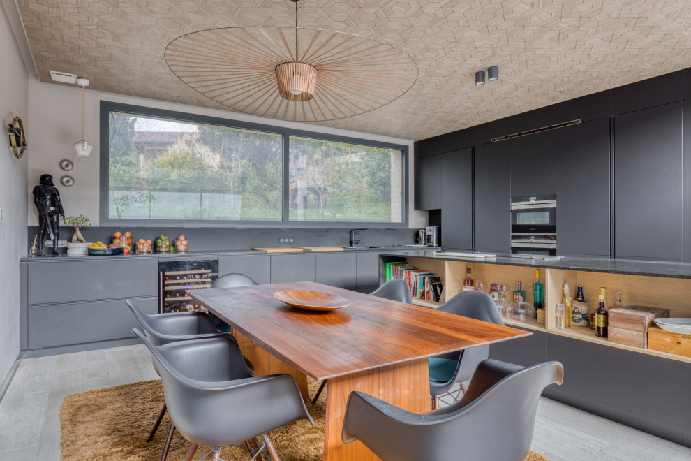 Стильный дизайн: угловая кухня-гостиная с плоскими фасадами, серыми фасадами, черной техникой, островом, серым полом и серой столешницей - последний тренд