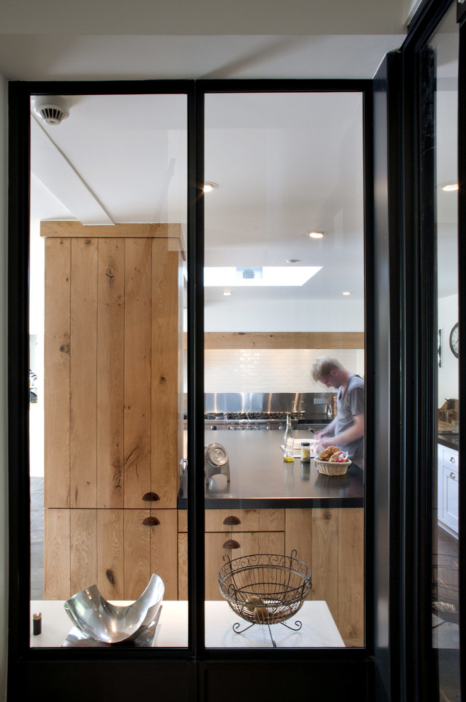 Cette image montre une cuisine ouverte noire et bois chalet en L et bois brun avec un placard à porte plane, un électroménager noir, îlot et plan de travail noir.