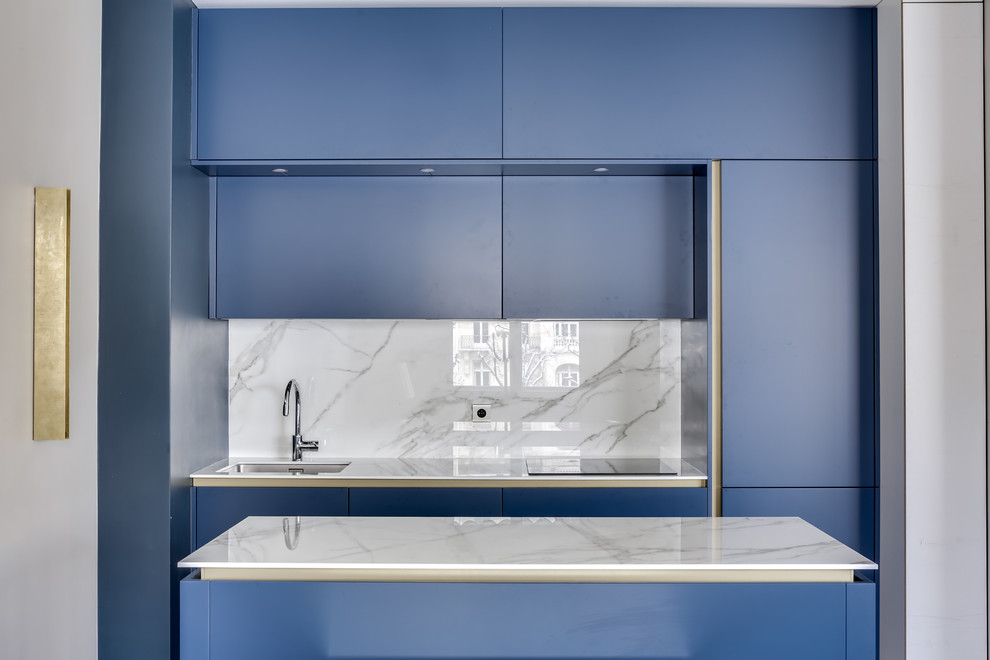 Cette photo montre une cuisine linéaire tendance avec un évier encastré, un placard à porte plane, des portes de placard bleues, une crédence grise, îlot et un plan de travail gris.