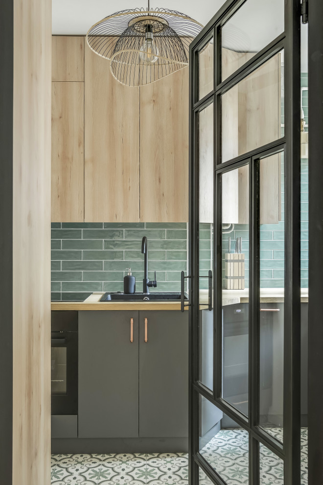Inspiration för ett avskilt, litet industriellt brun linjärt brunt kök, med en enkel diskho, luckor med profilerade fronter, skåp i ljust trä, träbänkskiva, grönt stänkskydd, stänkskydd i tunnelbanekakel, integrerade vitvaror, cementgolv och grönt golv