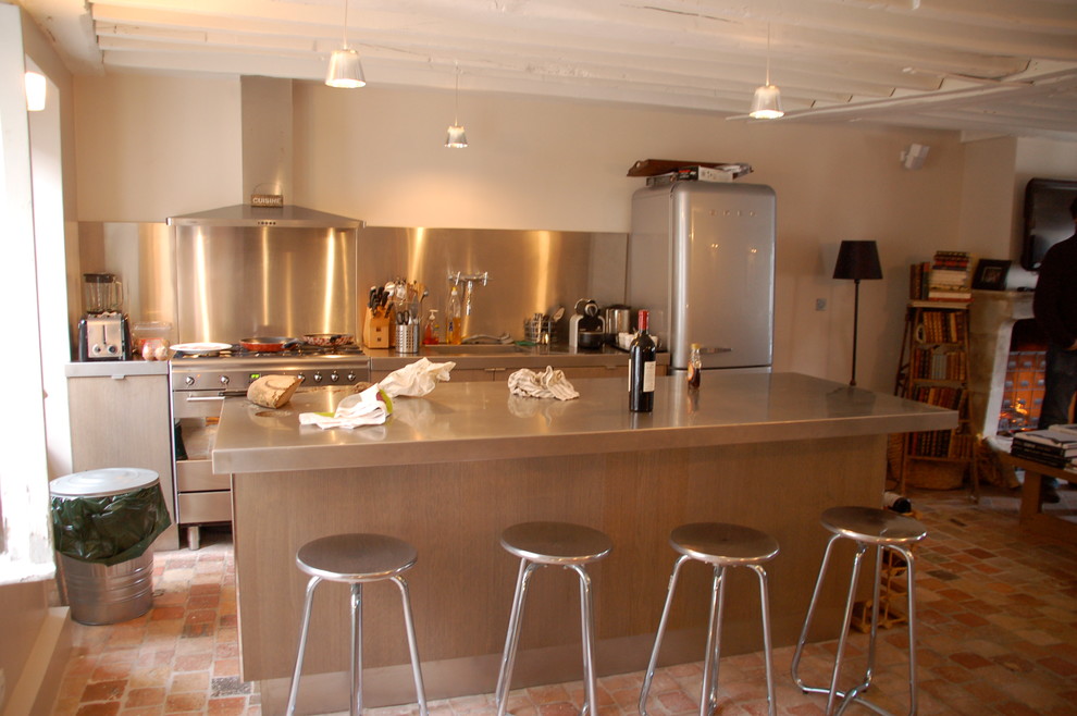 パリにあるカントリー風のおしゃれなアイランドキッチン (一体型シンク、ステンレスカウンター、シルバーの調理設備、テラコッタタイルの床) の写真