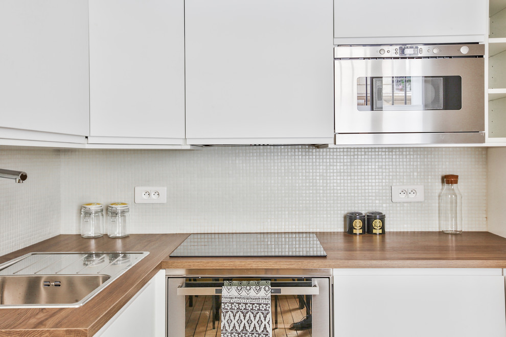 Bild på ett litet funkis brun brunt kök, med en enkel diskho, vita skåp, träbänkskiva, vitt stänkskydd, rostfria vitvaror, mellanmörkt trägolv, brunt golv och stänkskydd i mosaik