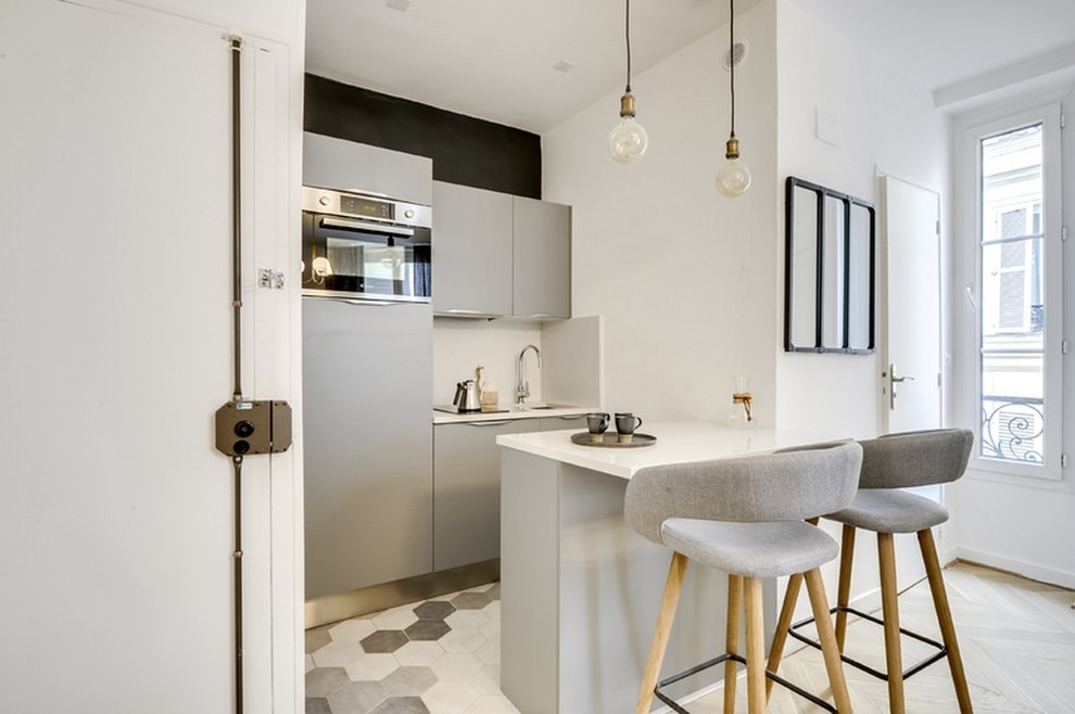 Inspiration for a small modern galley cement tile floor and gray floor open concept kitchen remodel in Paris with quartzite countertops, an island, an integrated sink, flat-panel cabinets, gray cabinets, white backsplash, stainless steel appliances and white countertops
