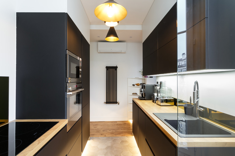 Example of a trendy galley medium tone wood floor and brown floor kitchen design in Paris with a drop-in sink, flat-panel cabinets, black cabinets, wood countertops, black backsplash, black appliances and beige countertops