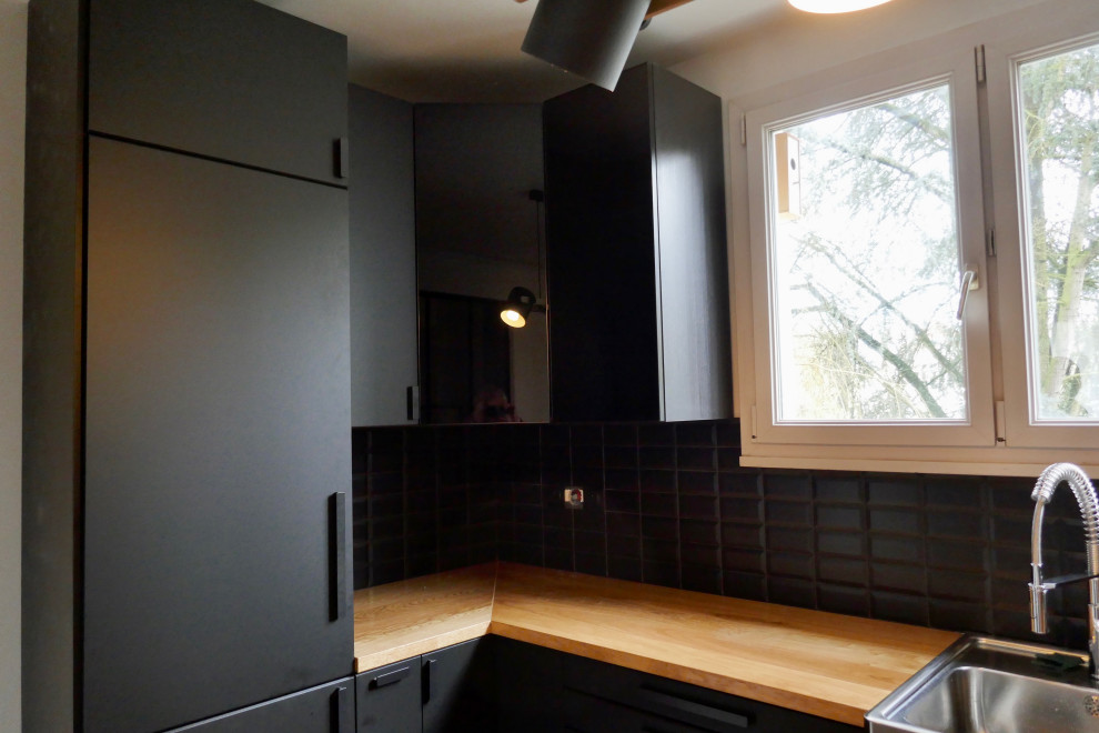パリにある高級な中くらいなモダンスタイルのおしゃれなキッチン (ドロップインシンク、フラットパネル扉のキャビネット、黒いキャビネット、木材カウンター、黒いキッチンパネル、サブウェイタイルのキッチンパネル、シルバーの調理設備、クッションフロア、茶色い床、茶色いキッチンカウンター) の写真
