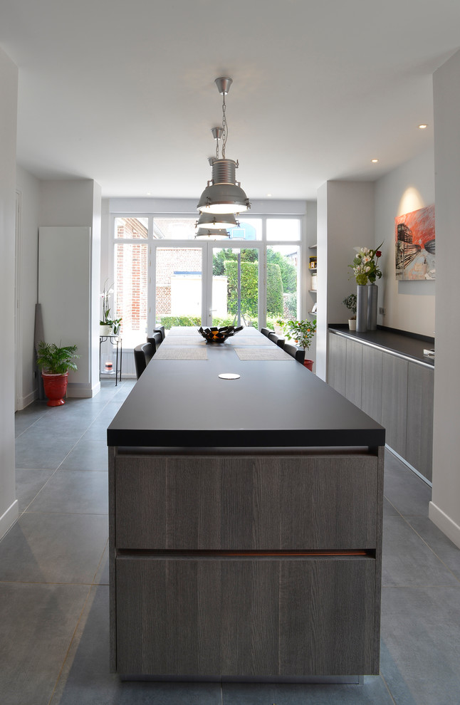 Inspiration for a large contemporary single-wall open plan kitchen in Paris with a built-in sink, beaded cabinets, dark wood cabinets, composite countertops, black splashback, black appliances, cement flooring, an island, grey floors and black worktops.