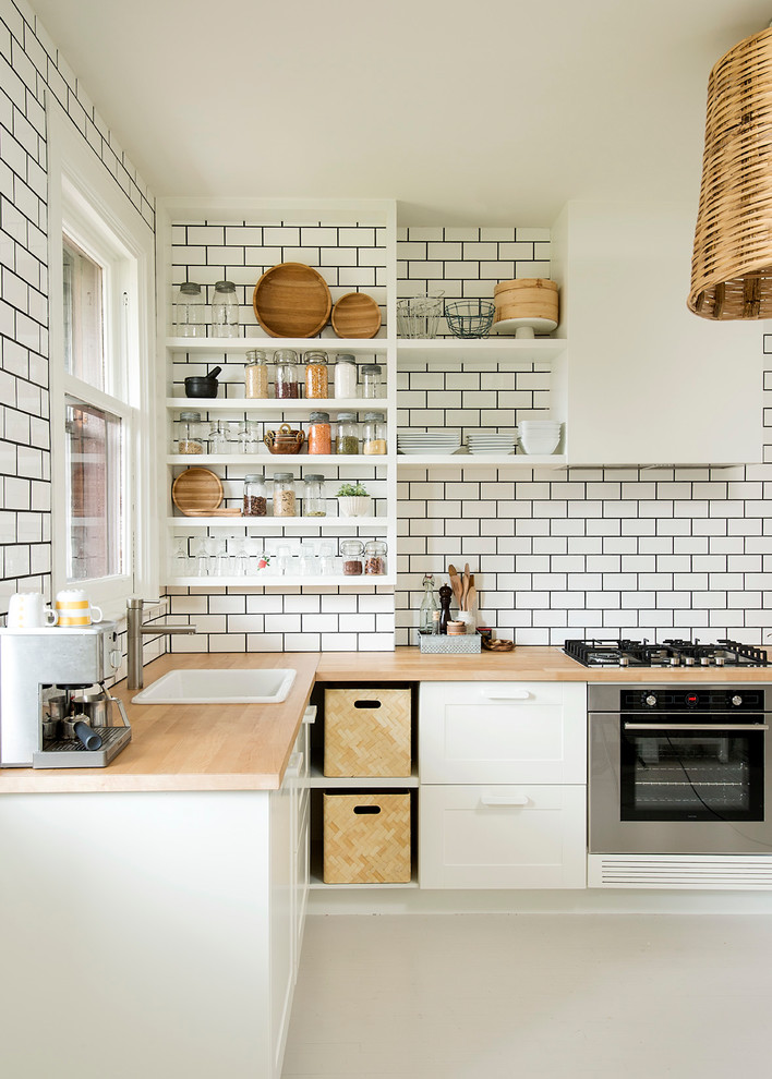 Klassisk inredning av ett kök, med en nedsänkt diskho, luckor med infälld panel, vita skåp, vitt stänkskydd, stänkskydd i tunnelbanekakel och rostfria vitvaror