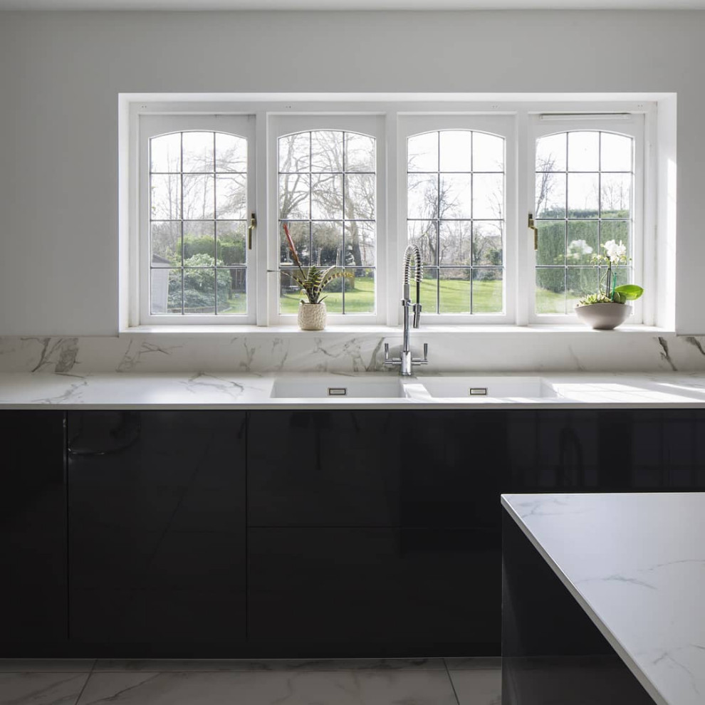 Immagine di una grande cucina minimal con lavello sottopiano, ante a filo, ante nere, top in superficie solida, paraspruzzi bianco, elettrodomestici da incasso, pavimento in marmo e top bianco