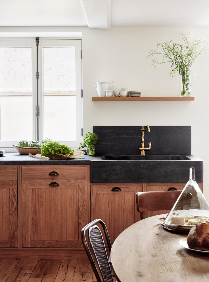 Einzeilige, Große Country Wohnküche mit integriertem Waschbecken, hellbraunen Holzschränken, Küchenrückwand in Schwarz und braunem Holzboden in Paris