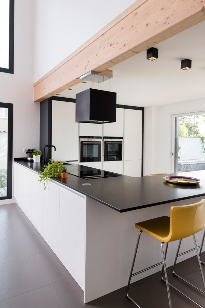 Cette image montre une cuisine design en U avec un placard à porte plane, des portes de placard blanches, un électroménager en acier inoxydable, une péninsule et un sol noir.