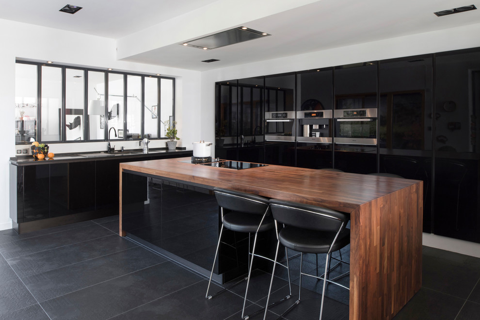 Exempel på ett modernt kök, med en undermonterad diskho, släta luckor, svarta skåp, träbänkskiva, fönster som stänkskydd, rostfria vitvaror, en köksö och svart golv