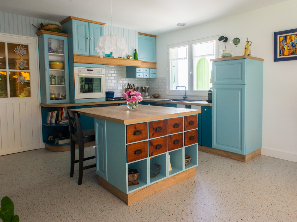Inredning av ett lantligt mellanstort brun brunt kök, med en enkel diskho, blå skåp, laminatbänkskiva, vitt stänkskydd, stänkskydd i tunnelbanekakel, vita vitvaror, terrazzogolv, en köksö och flerfärgat golv