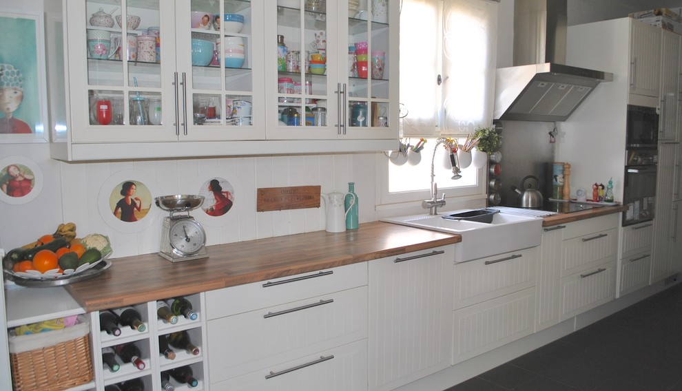 Modern inredning av ett stort linjärt kök med öppen planlösning, med en dubbel diskho, vita skåp, träbänkskiva, rostfria vitvaror och skiffergolv
