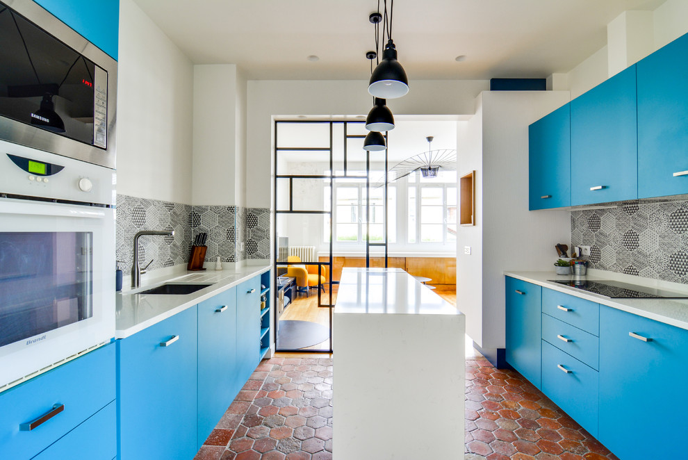 Inspiration pour une cuisine parallèle design fermée avec un évier encastré, un placard à porte plane, des portes de placard bleues, une crédence verte, un sol en brique, îlot, un sol rouge et un plan de travail blanc.