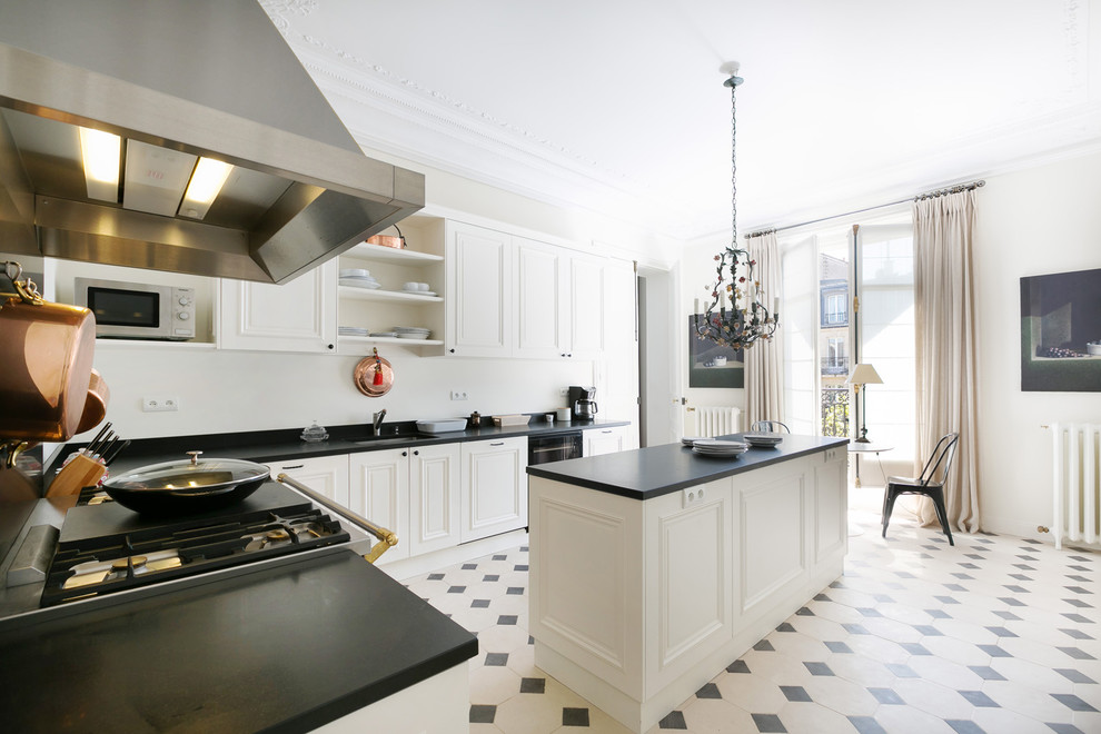 Große, Geschlossene Klassische Küche in L-Form mit weißen Schränken, Küchenrückwand in Schwarz, Elektrogeräten mit Frontblende und Kücheninsel in Paris