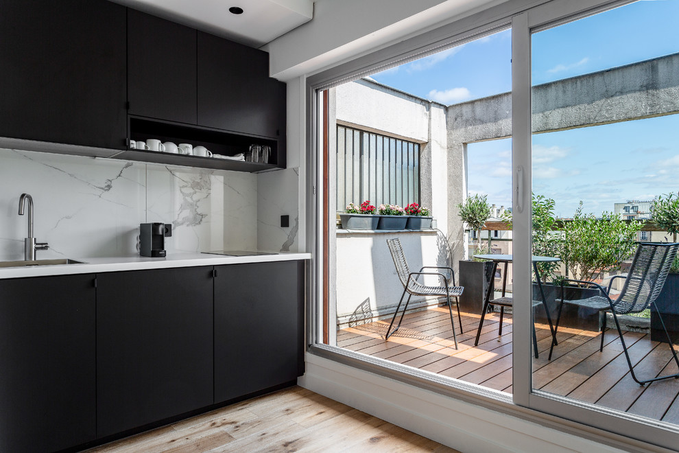 This is an example of a small contemporary single-wall open plan kitchen in London with a built-in sink, flat-panel cabinets, black cabinets, white splashback, light hardwood flooring, no island, beige floors, white worktops, marble worktops, marble splashback and integrated appliances.