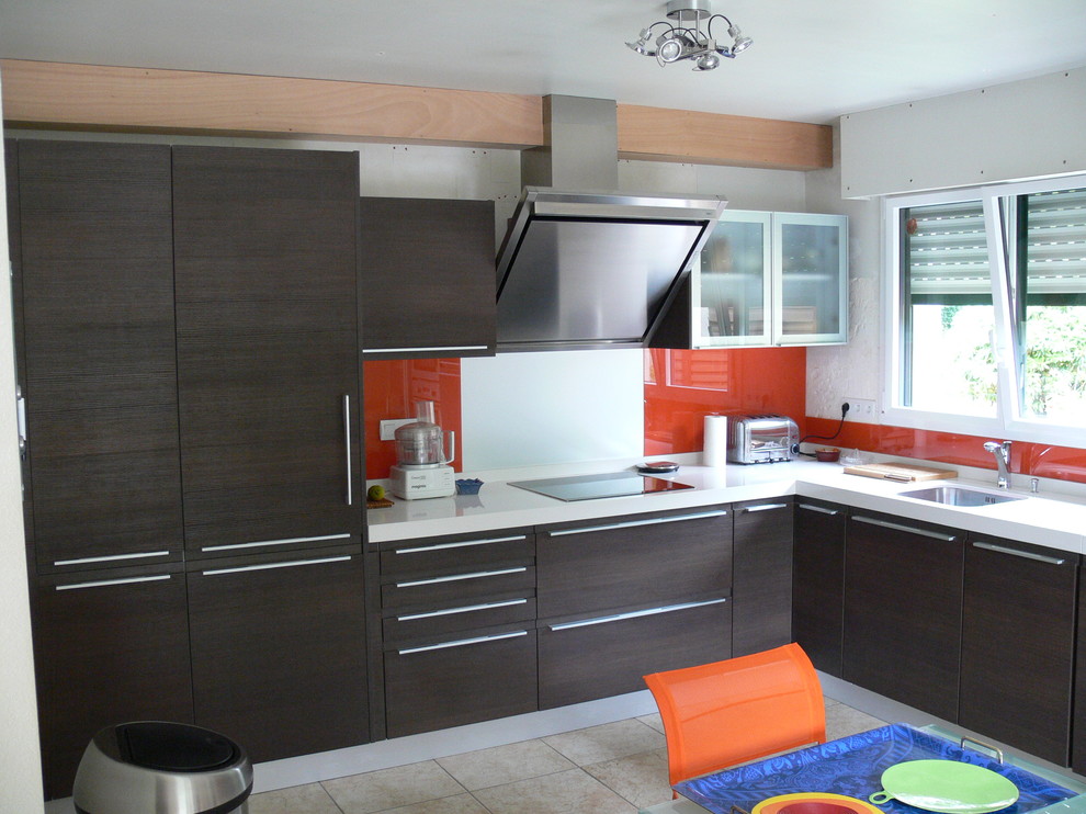 Пример оригинального дизайна: большая угловая кухня-гостиная в современном стиле с оранжевым фартуком, фартуком из стеклянной плитки и темными деревянными фасадами без острова