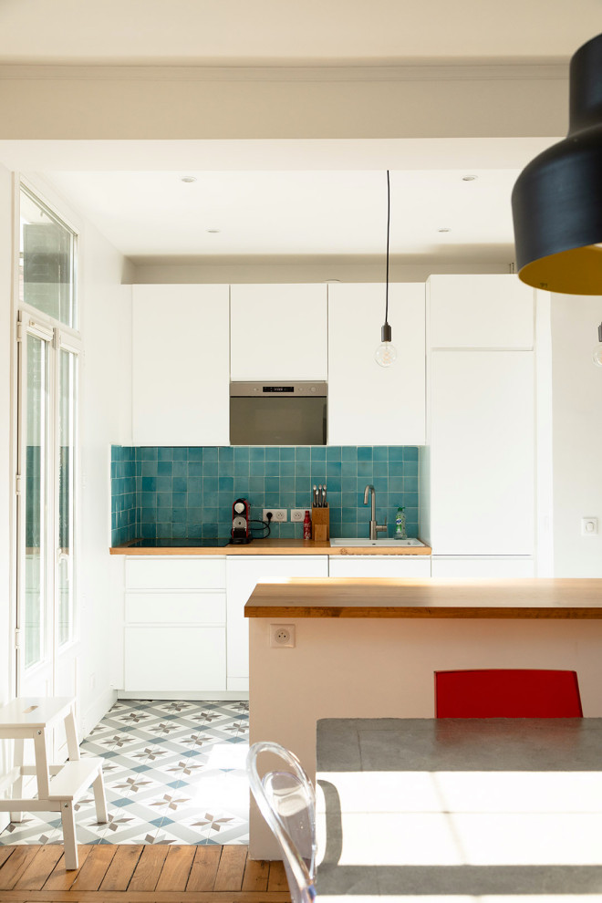 Exempel på ett litet modernt beige beige kök, med en nedsänkt diskho, släta luckor, vita skåp, träbänkskiva, blått stänkskydd, stänkskydd i terrakottakakel, integrerade vitvaror, cementgolv, en köksö och flerfärgat golv