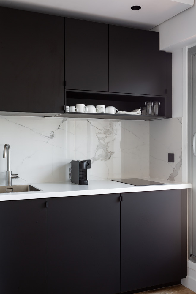 Inspiration för små moderna linjära vitt kök med öppen planlösning, med en enkel diskho, släta luckor, svarta skåp, laminatbänkskiva, vitt stänkskydd, stänkskydd i marmor, integrerade vitvaror och ljust trägolv