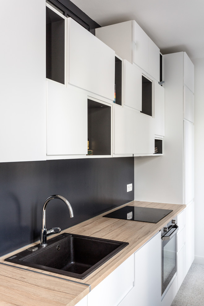 Example of a mid-sized minimalist single-wall vinyl floor and gray floor open concept kitchen design in Paris with wood countertops, a drop-in sink, flat-panel cabinets, white cabinets, black backsplash, slate backsplash, black appliances, no island and beige countertops
