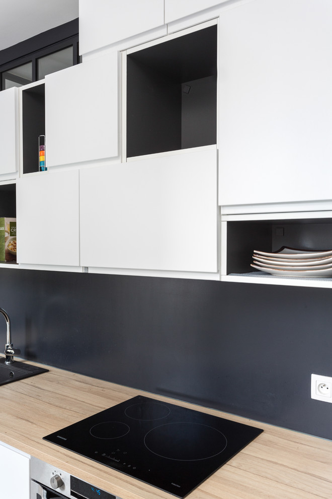 Design ideas for a medium sized modern single-wall open plan kitchen in Paris with wood worktops, a built-in sink, flat-panel cabinets, white cabinets, black splashback, slate splashback, black appliances, vinyl flooring, no island, grey floors and beige worktops.