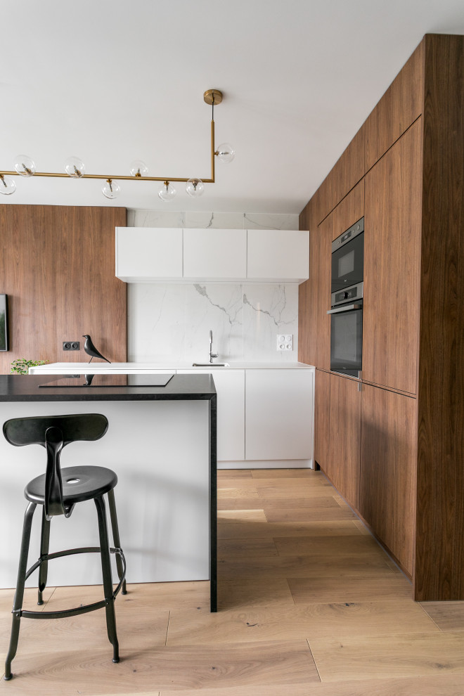 Large contemporary l-shaped kitchen/diner in Paris with a submerged sink, flat-panel cabinets, white cabinets, granite worktops, white splashback, marble splashback, black appliances, light hardwood flooring, an island, brown floors and black worktops.