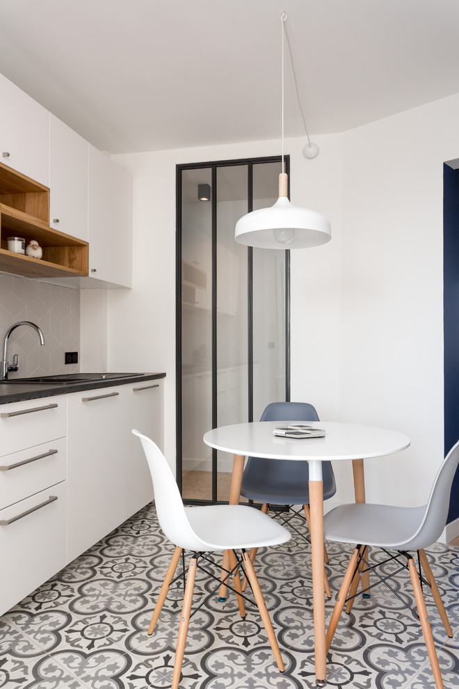 Inspiration for a mid-sized modern galley gray floor and cement tile floor enclosed kitchen remodel in Paris with white cabinets, gray backsplash, ceramic backsplash, a drop-in sink, flat-panel cabinets, solid surface countertops, stainless steel appliances, no island and black countertops