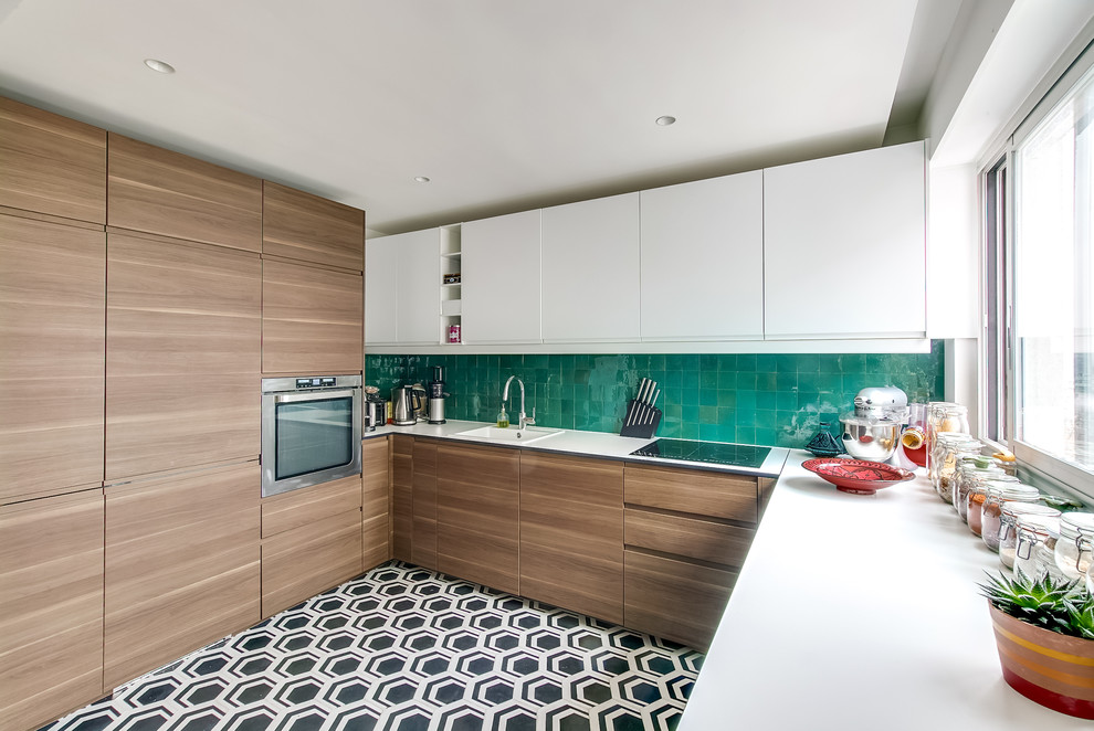 This is an example of a medium sized contemporary u-shaped open plan kitchen in Paris with green splashback, terracotta splashback, stainless steel appliances, cement flooring, a built-in sink, flat-panel cabinets, white cabinets, multi-coloured floors and laminate countertops.