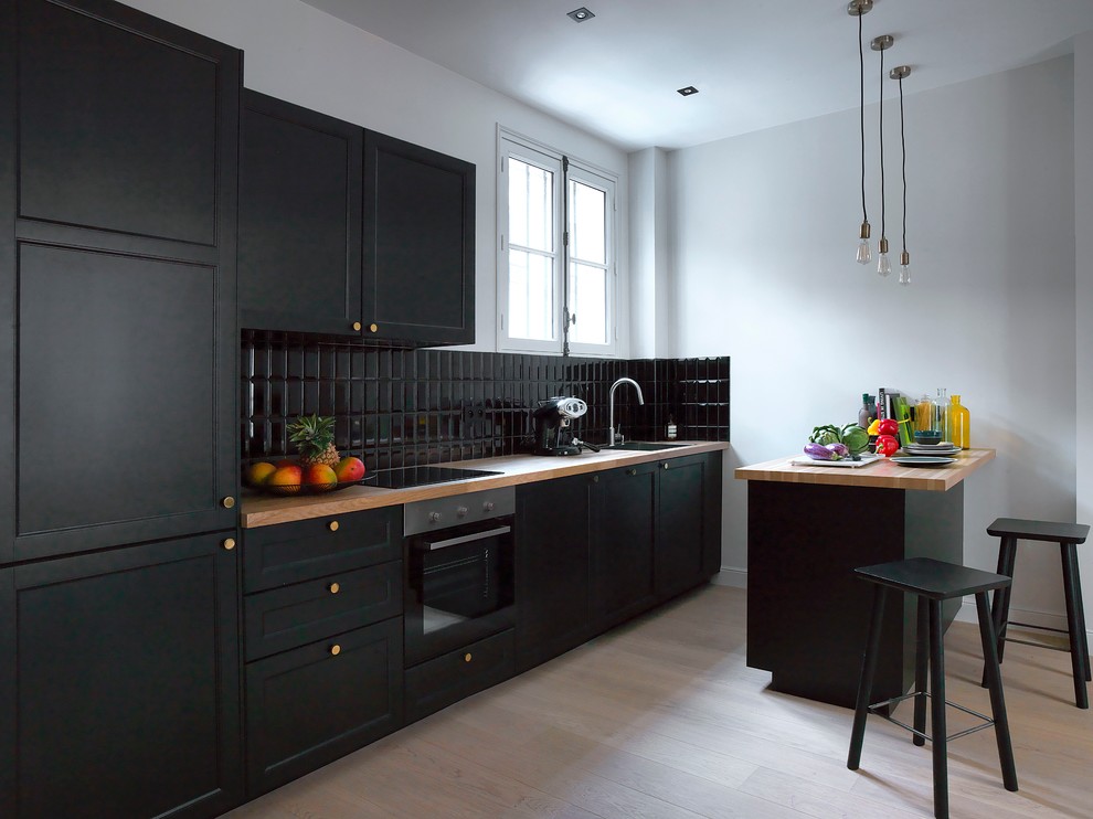 Photo of a medium sized traditional galley open plan kitchen in Paris with recessed-panel cabinets, wood worktops, black splashback, metro tiled splashback, stainless steel appliances, light hardwood flooring, a breakfast bar and a submerged sink.