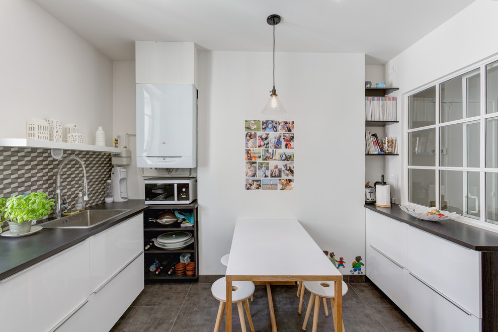 Inspiration for a mid-sized scandinavian l-shaped cement tile floor and gray floor enclosed kitchen remodel in Paris with brown backsplash, brown countertops, a drop-in sink, flat-panel cabinets, white cabinets, laminate countertops, cement tile backsplash, black appliances and a peninsula