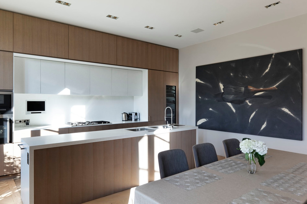 Zweizeilige, Große Moderne Küche mit Doppelwaschbecken, Küchenrückwand in Weiß, hellem Holzboden, Kücheninsel und dunklen Holzschränken in Paris