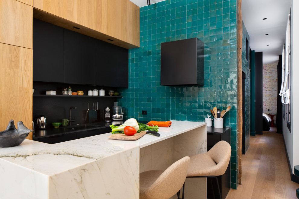 Cette image montre une cuisine design avec un évier encastré, des portes de placard noires, un plan de travail en granite, une crédence verte, une crédence en terre cuite, un électroménager noir et plan de travail noir.