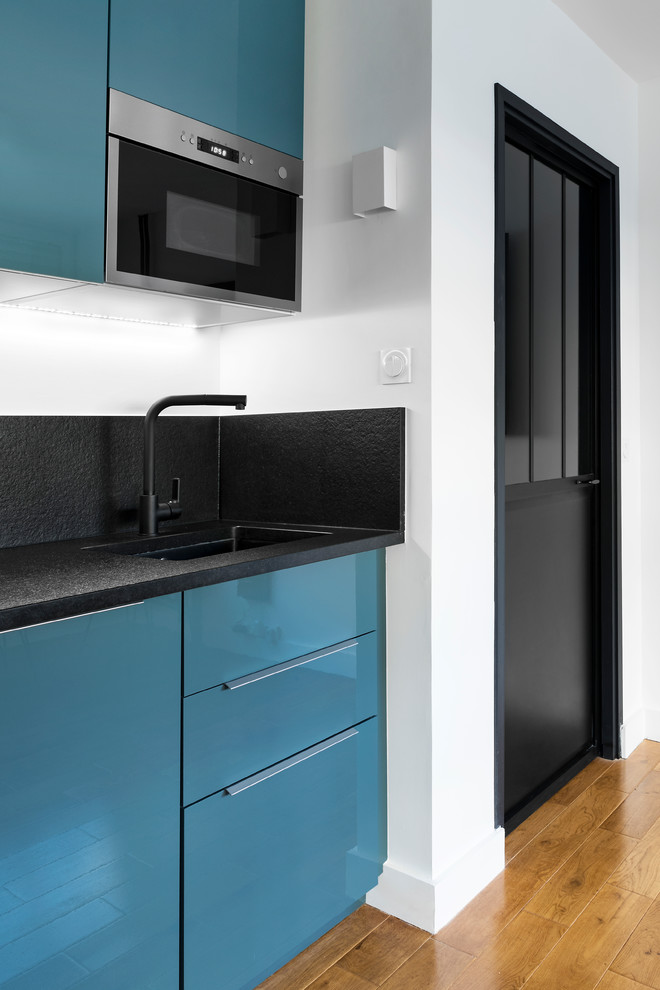 Skandinavisk inredning av ett litet svart linjärt svart kök och matrum, med luckor med profilerade fronter, blå skåp, granitbänkskiva, en undermonterad diskho, svart stänkskydd, integrerade vitvaror och mellanmörkt trägolv